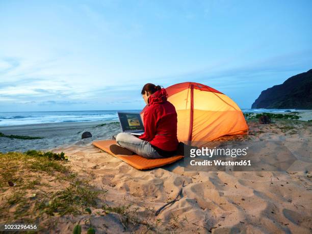 usa, hawaii, kauai, polihale state park, woman using laptop at tent on the beach at dusk - remote location stock-fotos und bilder