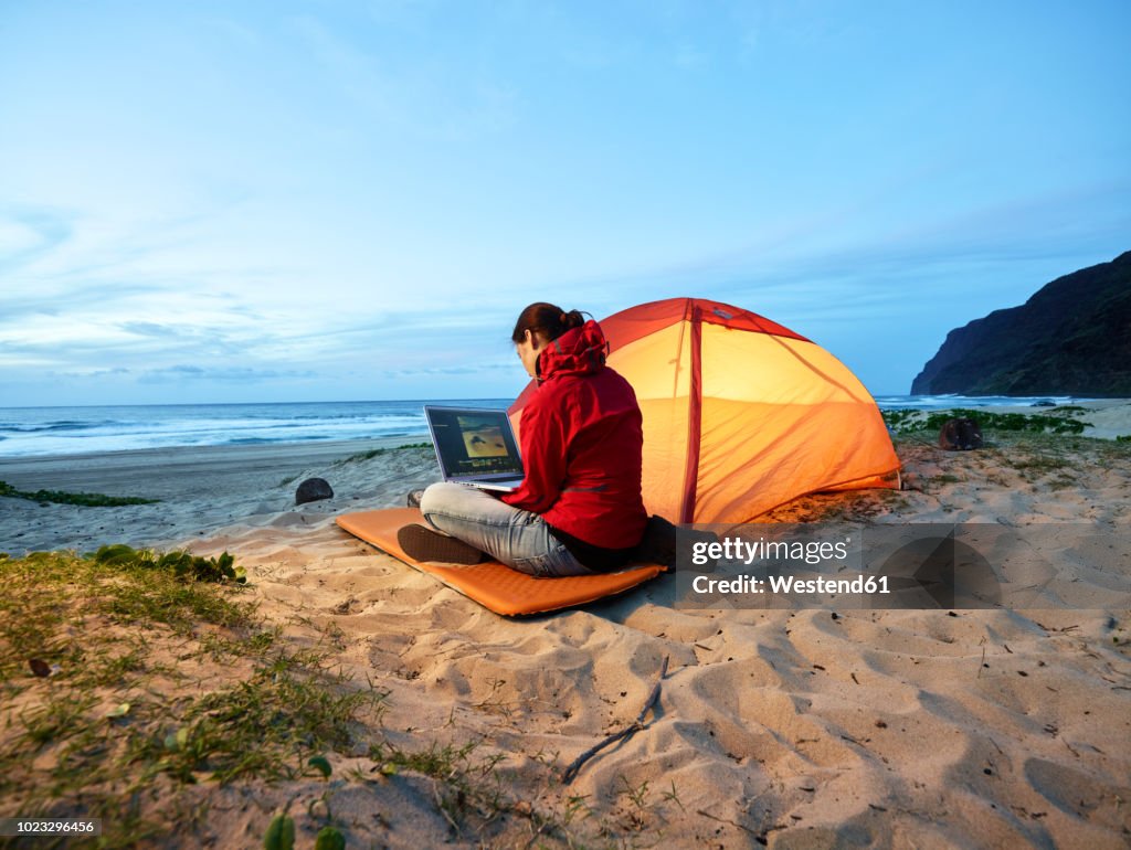 USA, Hawaii, Kauai, Polihale State Park, woman using laptop at tent on the beach at dusk