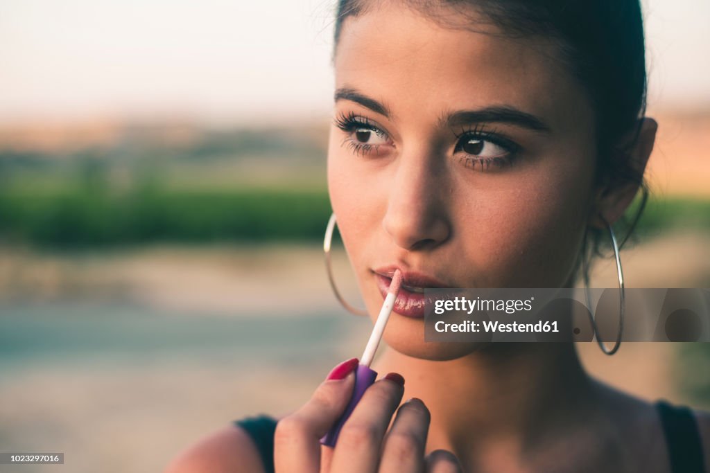 Portrait of teenage girl in nature applying lip gloss