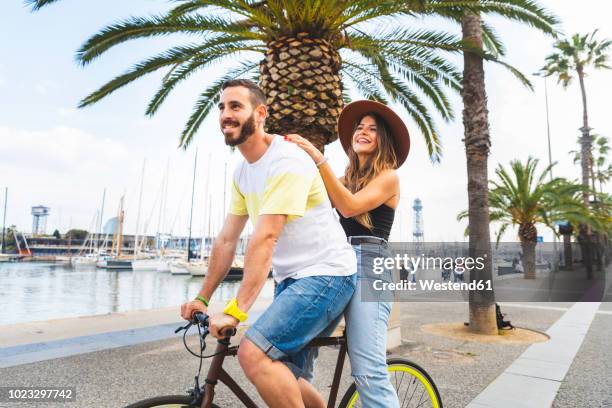 spain, barcelona, couple having fun and sharing a ride on a bike together on seaside promenade - promenade stockfoto's en -beelden