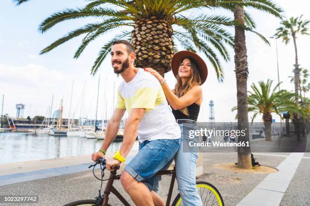 spain, barcelona, couple having fun and sharing a ride on a bike together on seaside promenade - promenade seafront stock pictures, royalty-free photos & images