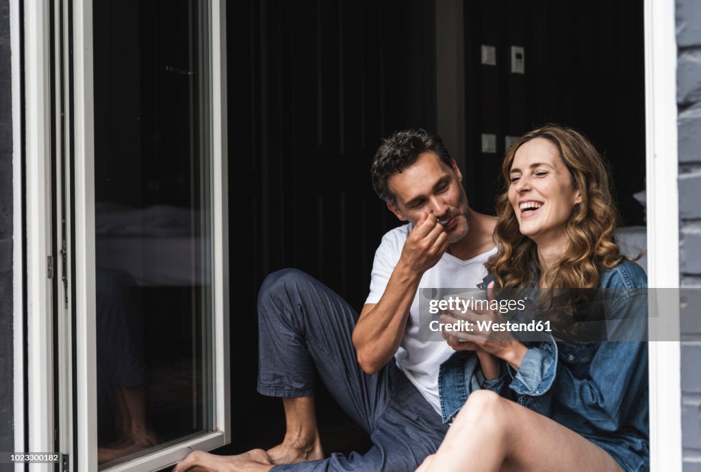 Happy couple in nightwear at home sitting at French window