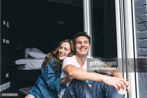 happy couple in nightwear at home sitting at french window - happy couple cuddle stockfoto's en -beelden