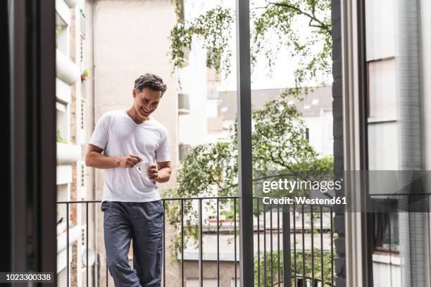 smiling man in pyjama with cup of coffee standing on balcony - pijama fotografías e imágenes de stock