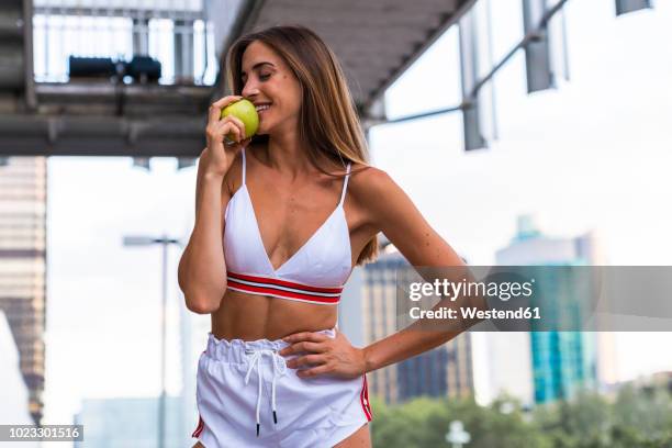 attractive young woman in sportswear eating an apple - slim skinny stock-fotos und bilder