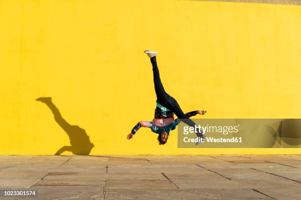 acrobat jumping somersaults in front of yellow wall - man flying stockfoto's en -beelden