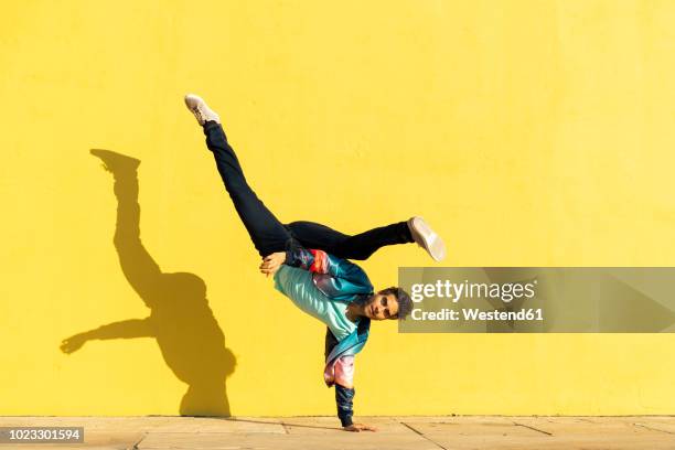 acrobat doing movement training in front of a yellow wall - breakdance stock-fotos und bilder