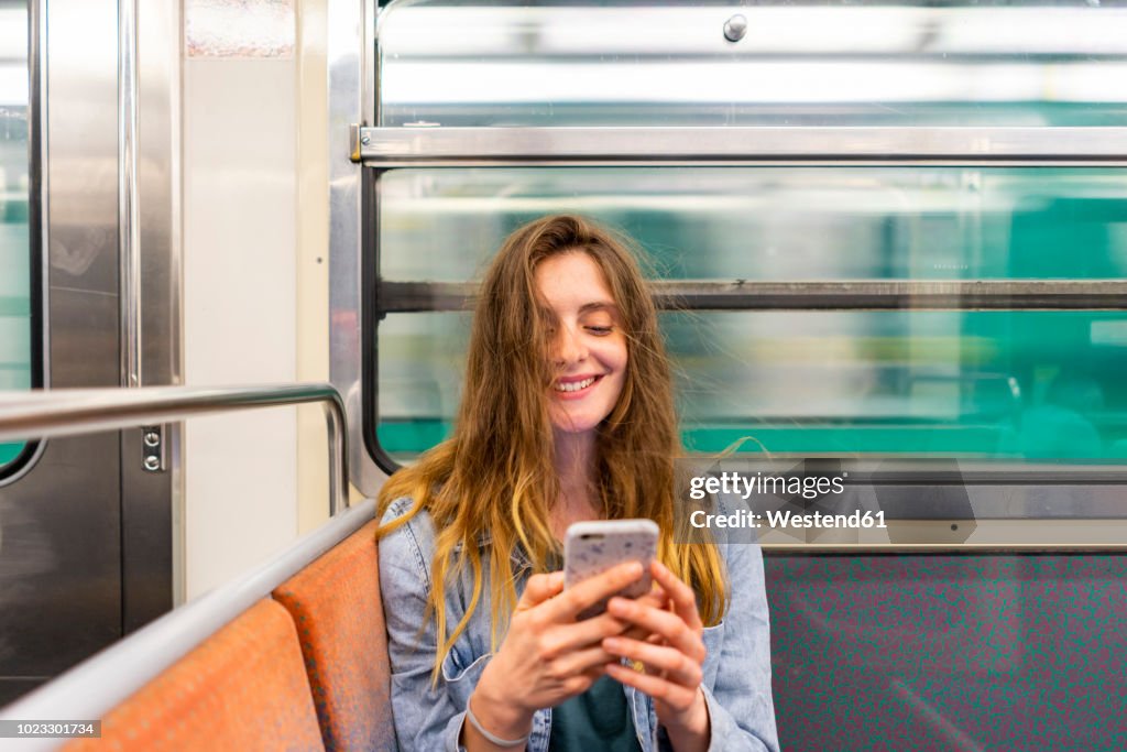 Portrait of smiling young woman in underground train looking at smartphone