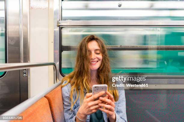 portrait of smiling young woman in underground train looking at smartphone - train vehicle stock pictures, royalty-free photos & images