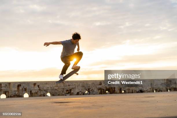 young chinese man skateboarding at sunsrise near the beach - skateboardfahren stock-fotos und bilder