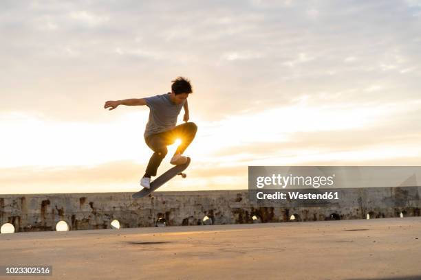 young chinese man skateboarding at sunsrise near the beach - skateboard foto e immagini stock