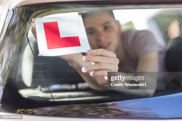 learner driver placing letter l on rear window of car - letter l stock pictures, royalty-free photos & images