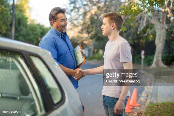 learner driver and instructor shaking hands at car - learning to drive stock-fotos und bilder
