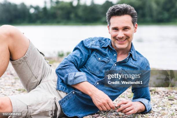 portrait of smiling man relaxing at the riverside - acostado de lado fotografías e imágenes de stock