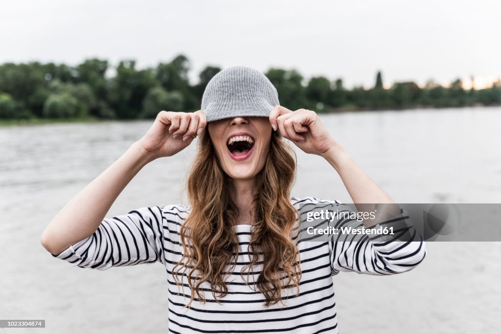 Laughing woman playing with wooly hat at a river