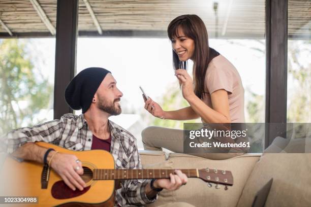 young man at home sitting on couch playing guitar for woman - cantare una serenata foto e immagini stock