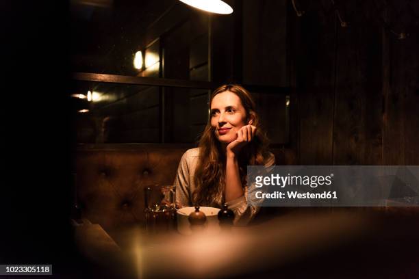 smiling woman sitting at dining table looking sideways - dating stock-fotos und bilder
