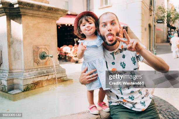 france, aix-en-provence, funny toddler girl and father with tongue out next to a fountain in the city - family portrait humor fotografías e imágenes de stock