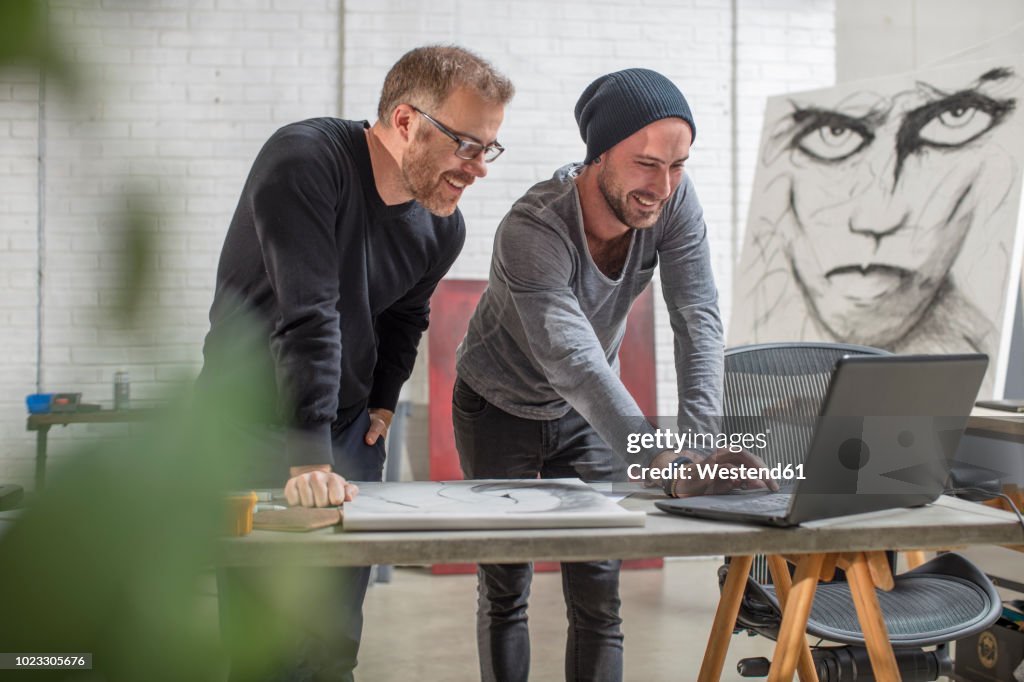 Smiling artist using laptop with man in studio