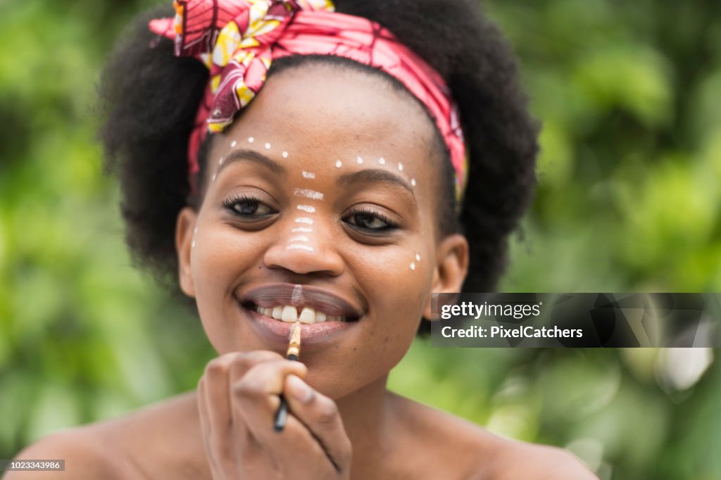 Close up young African woman paints traditional make up on her face