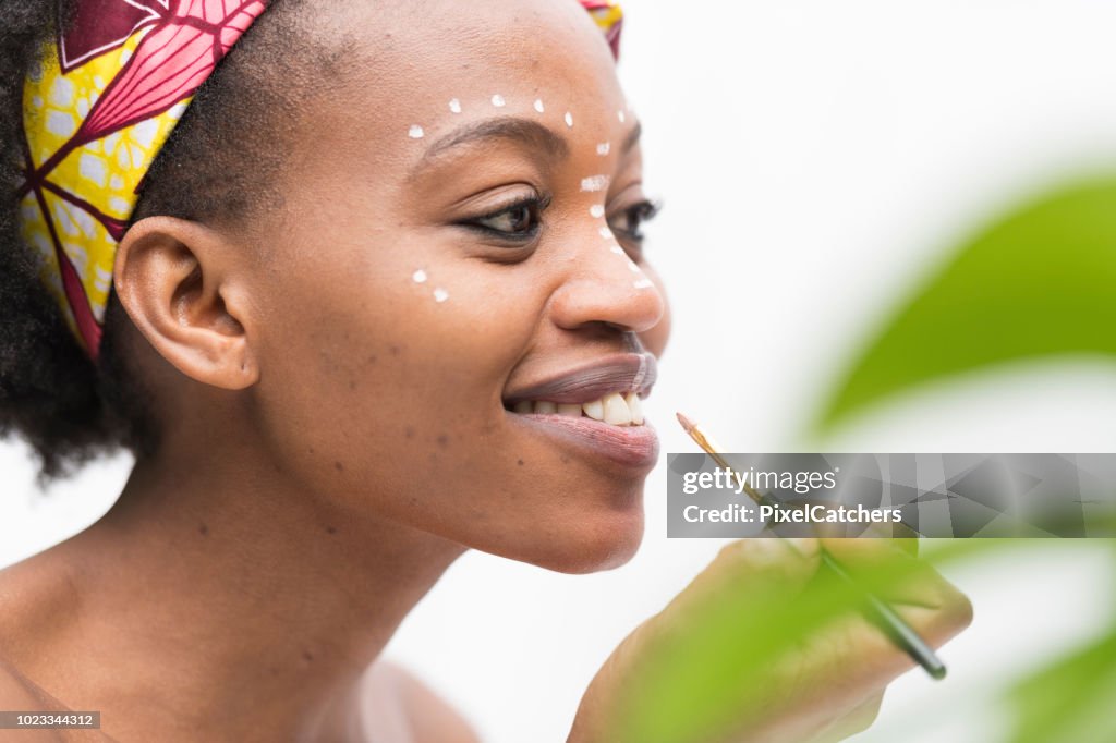 Profile portrait young African woman about to paint lips with traditional make up
