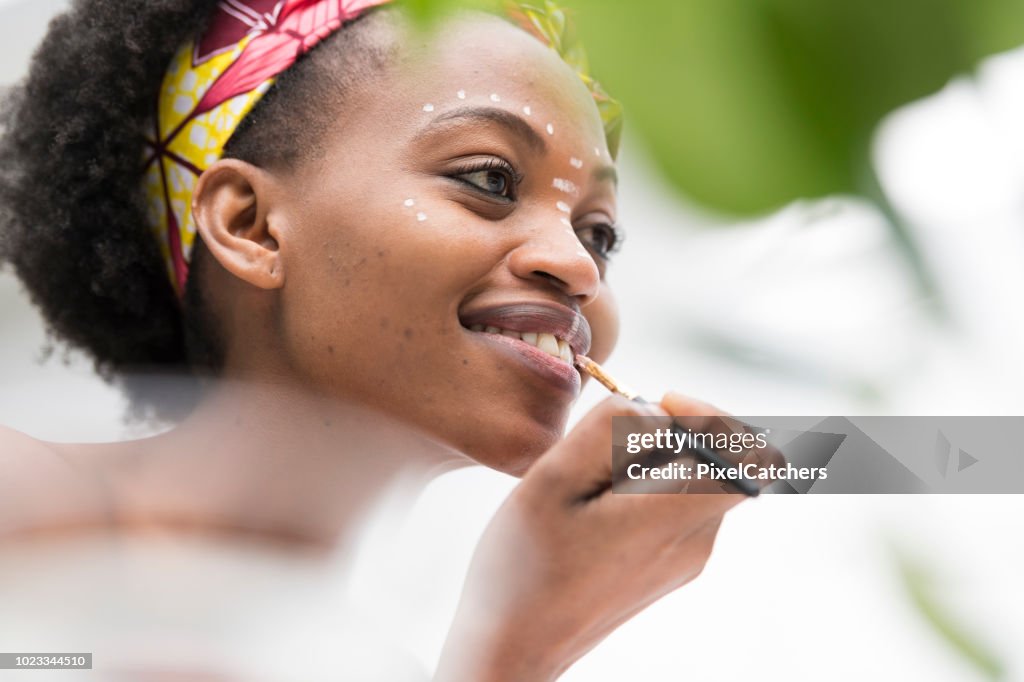 Low angle view young African woman paint traditional make up on her face