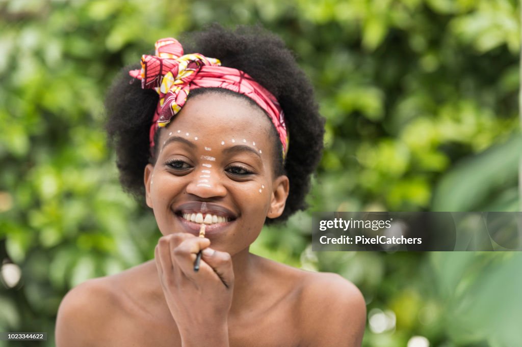 Young African woman painting calamine lotion on her lips traditional make up paterns
