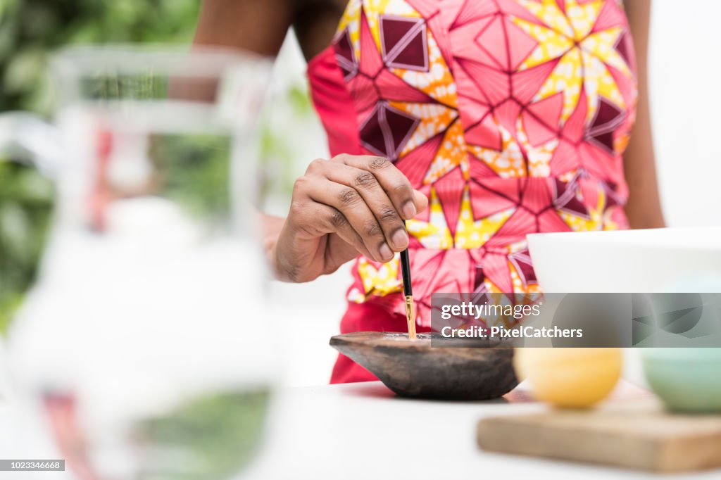 Cropped shot of young African woman as she dips brush into lotion for traditional face painting