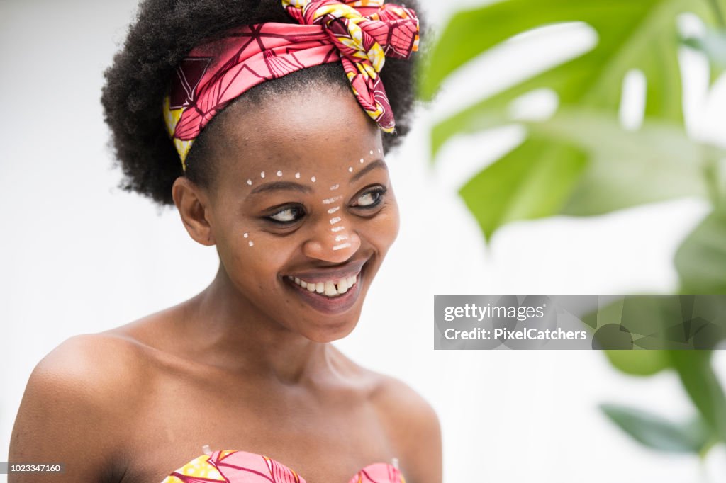Young African woman smiles at her reflection beautiful traditional make up on her face