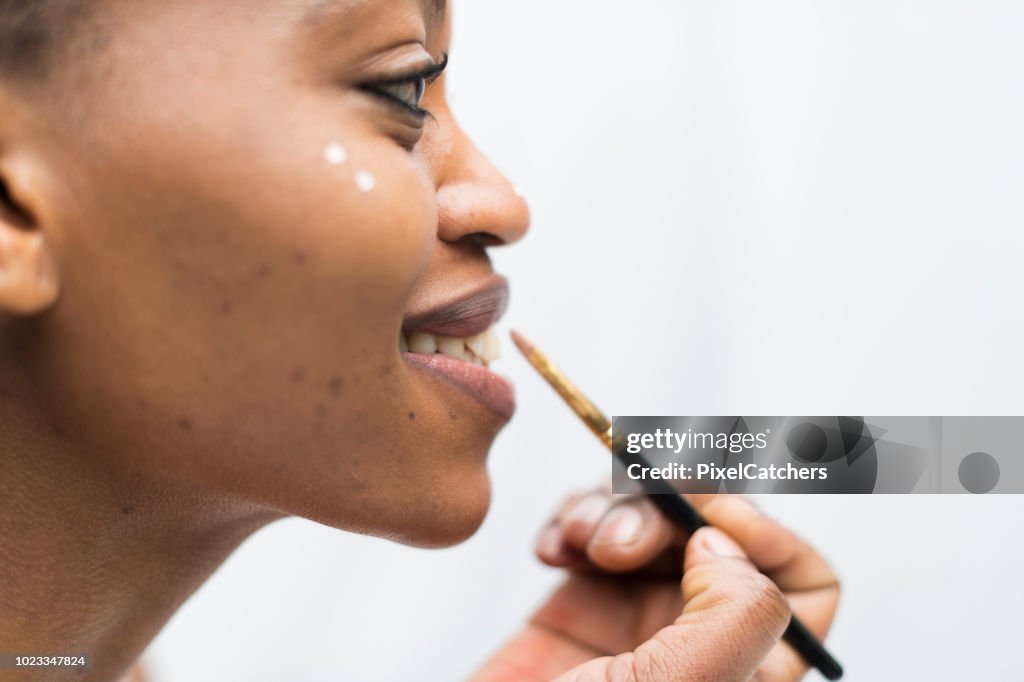 Profile close up young African woman paints traditional face paint on hep face