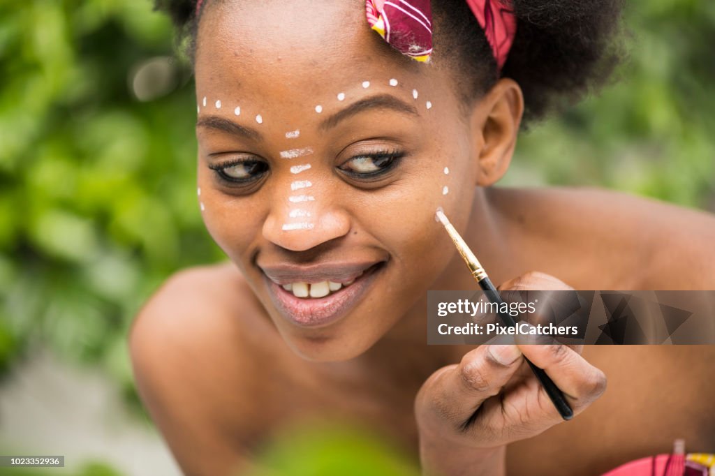Young African woman paints dots of traditional make up on her face