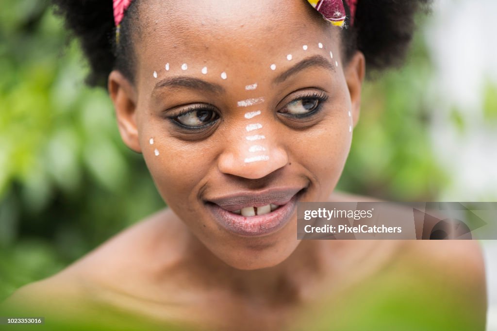 Close up portrait young African woman with traditional face paint sideways glance