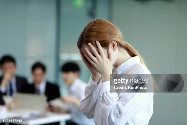 stressed businesswoman at desk,colleagues in background having discussion - 欲求不満 ストックフォトと画像