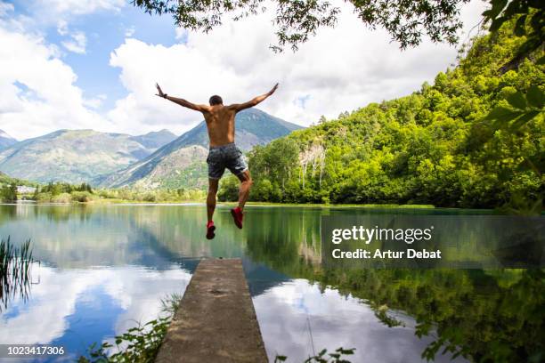 guy jumping with stunning mountain landscape reflected in the lake water. - moment of silence stock-fotos und bilder