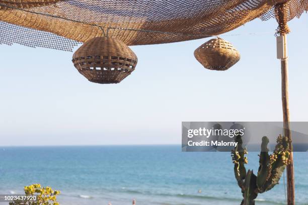 view on beach and water from balcony with lamps hanging from the awning. marrakesh, marrakesh-safi, morocco. - beach balcony stock pictures, royalty-free photos & images