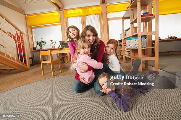germany, nursery, female nursery teacher and children playing together - maestra foto e immagini stock