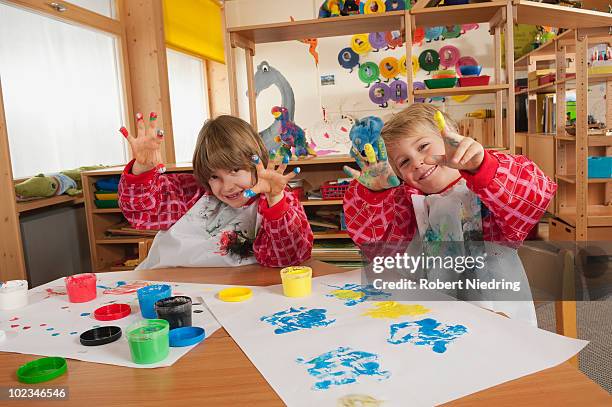 germany, two boys (3-4), (6-7) fingerpainting in nursery, showing hands, smiling, portrait - kids arts and crafts stock pictures, royalty-free photos & images