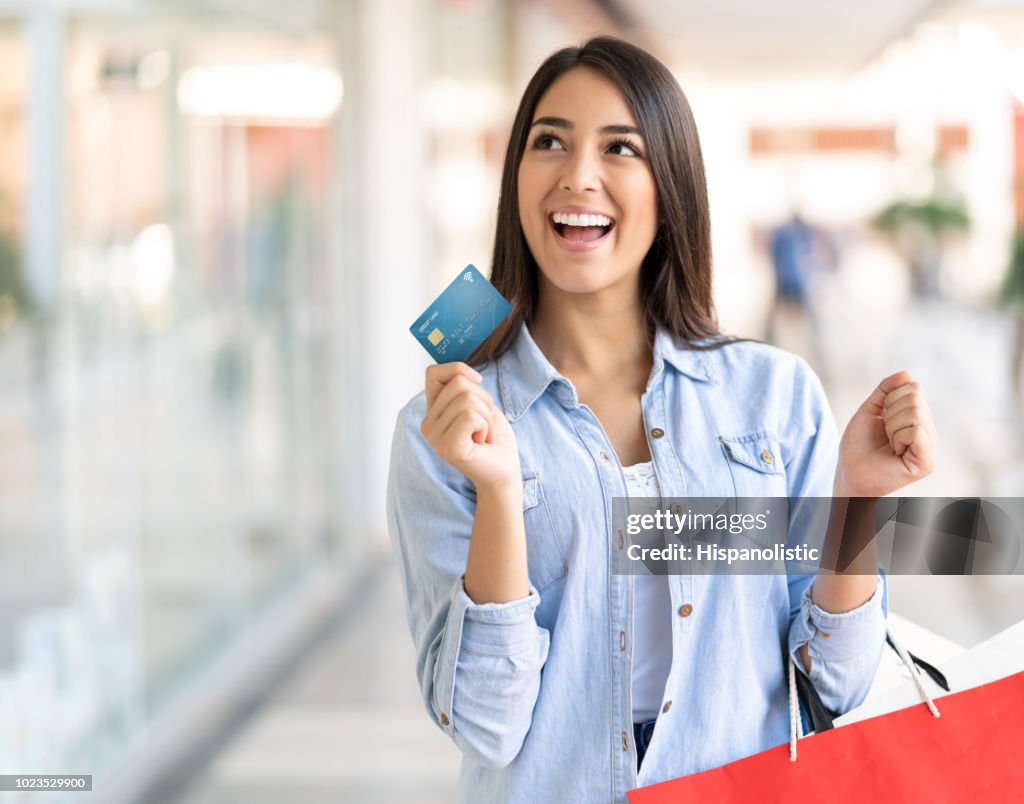 若い女性を探して離れた空想彼女のデビット カードとショッピング バッグを押しながら興奮してください。