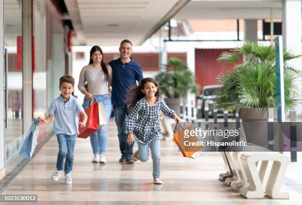latinamerikanska kärleksfull familj vid mall föräldrar gå långt efter och barn kör medan du håller kassar och påsar - latin american and hispanic shopping bags bildbanksfoton och bilder