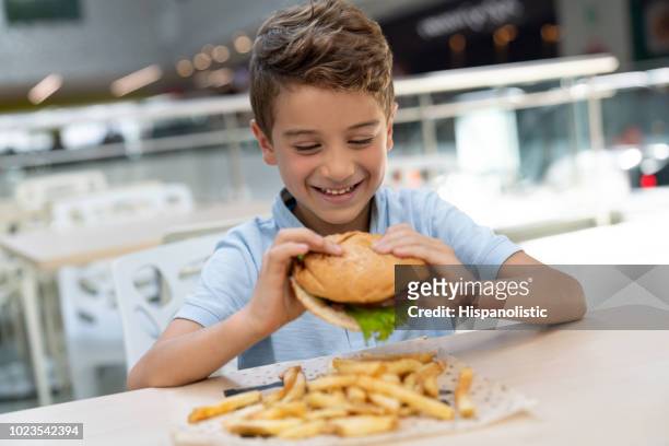 glada lilla pojke redo att njuta av en läcker hamburgare och pommes frites på foodcourt i ett köpcentrum - kid eating burger bildbanksfoton och bilder