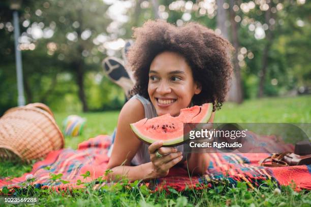 smiling woman holdinga  slice of watermelon on picnic and looking in distance - watermelon picnic stock pictures, royalty-free photos & images