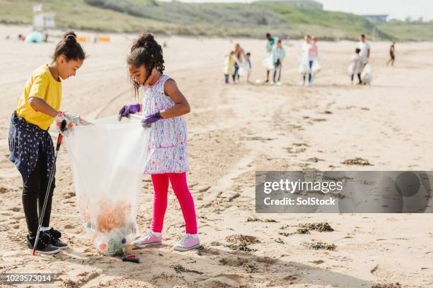 young girls collecting plastics and rubbish off a beach - beach clean up uk stock pictures, royalty-free photos & images