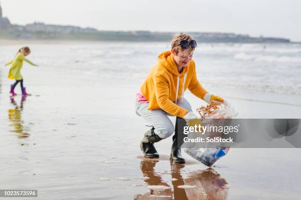 environmentally conscious woman cleans up beach - environmental cleanup stock pictures, royalty-free photos & images