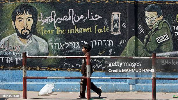 Palestinian boy walks past a mural depicting captured Israeli soldier Gilad Shalit and Ron Arad , an Israeli pilot who went missing when he flew a...