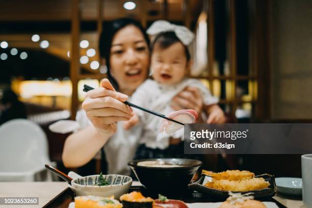 young asian mother and baby girl enjoying fresh sushi set joyfully in a japanese restaurant - asian baby eating stock pictures, royalty-free photos & images