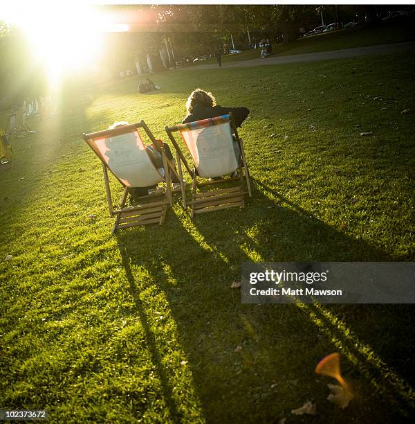 two people sitting in deckchairs in a park - deck chair stock pictures, royalty-free photos & images