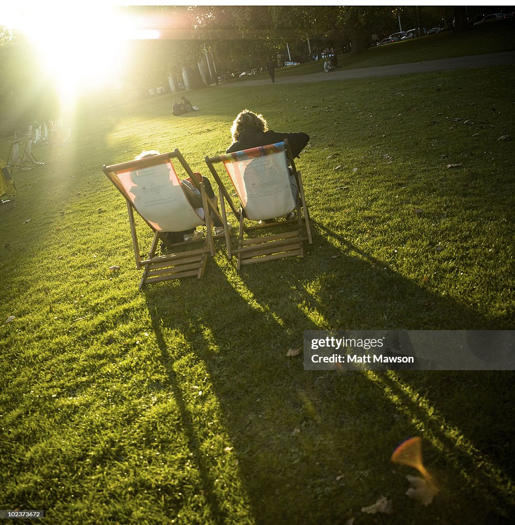 Two people sitting in deckchairs in a park