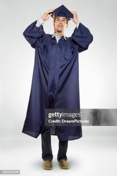 male high school graduate holding his cap - graduierten talar stock-fotos und bilder