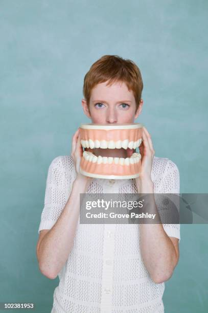 woman holding oversized teeth in front of her mout - gebiss mensch zähne stock-fotos und bilder