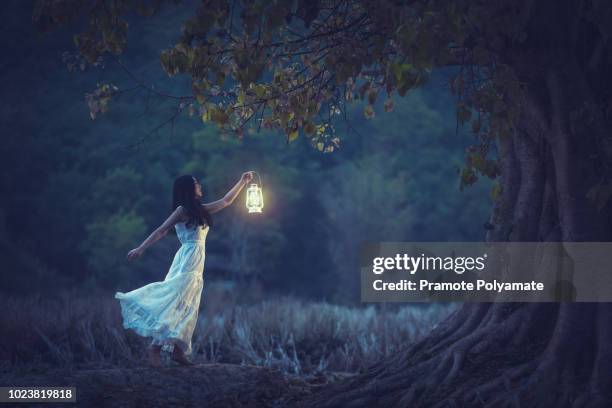 beautiful girl in white holding a lantern in the autumn forest shining under the trees. - blue candle stock-fotos und bilder